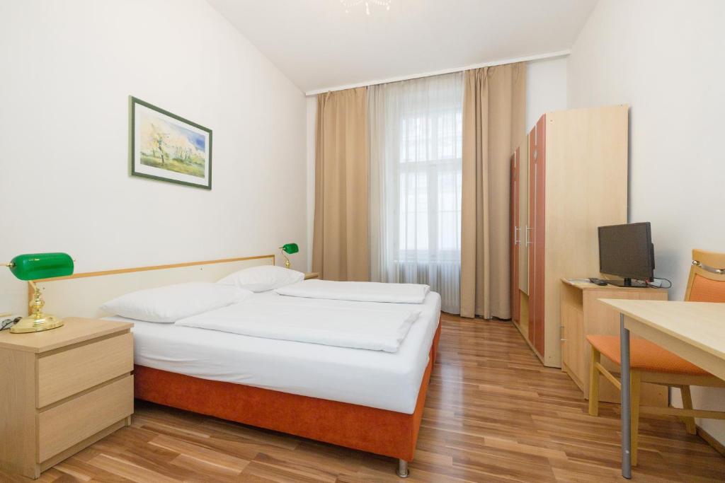 Schlafzimmer mit einem Bett, einem Schreibtisch und einem TV in der Unterkunft Pension Votiv in Wien