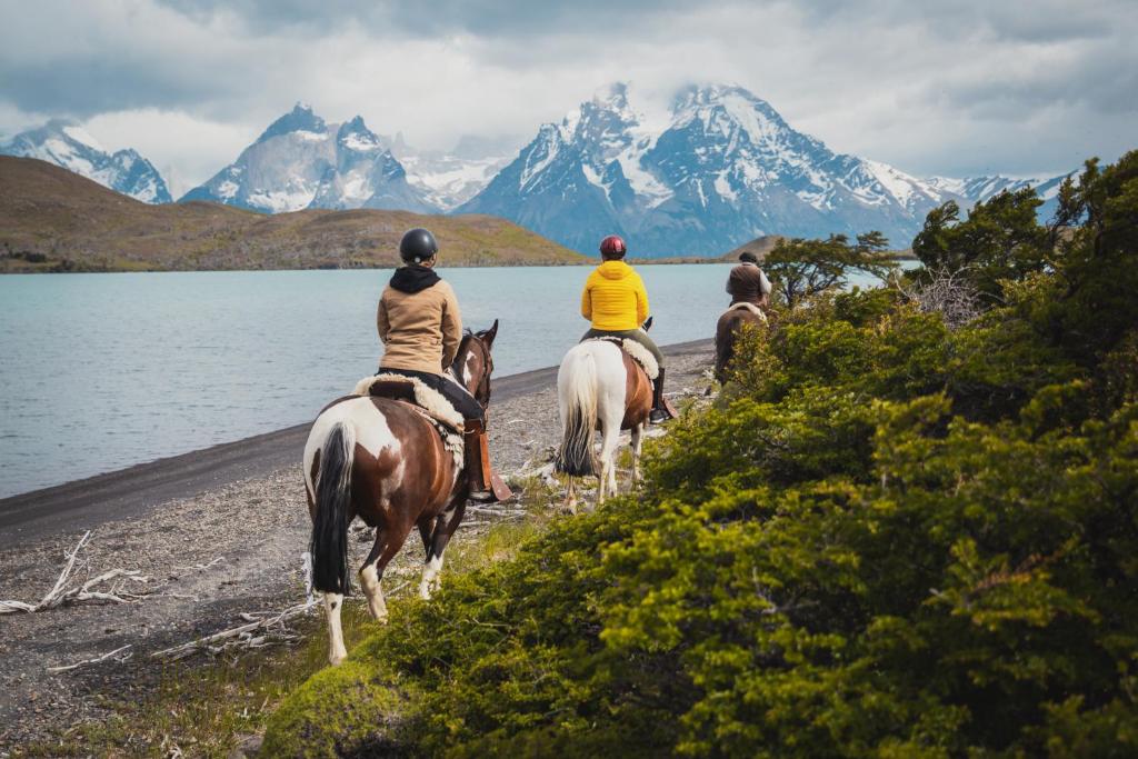 three people riding horses on a beach near the water at CABAÑA ESTANCIA LAZO in Torres del Paine
