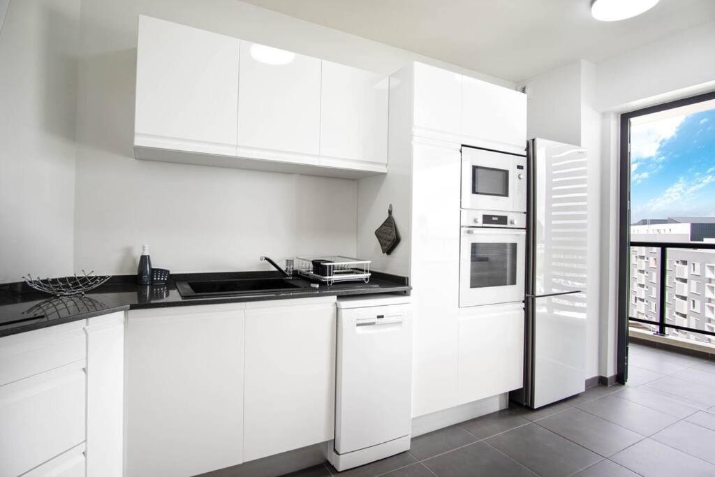a white kitchen with white cabinets and a large window at Appartement Corail Bleu in Fort-de-France