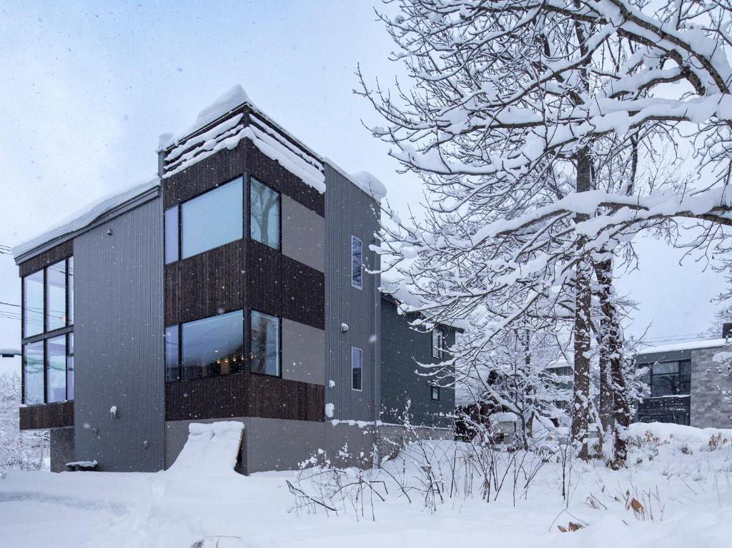 a building covered in snow next to a tree at Olaf House in Niseko