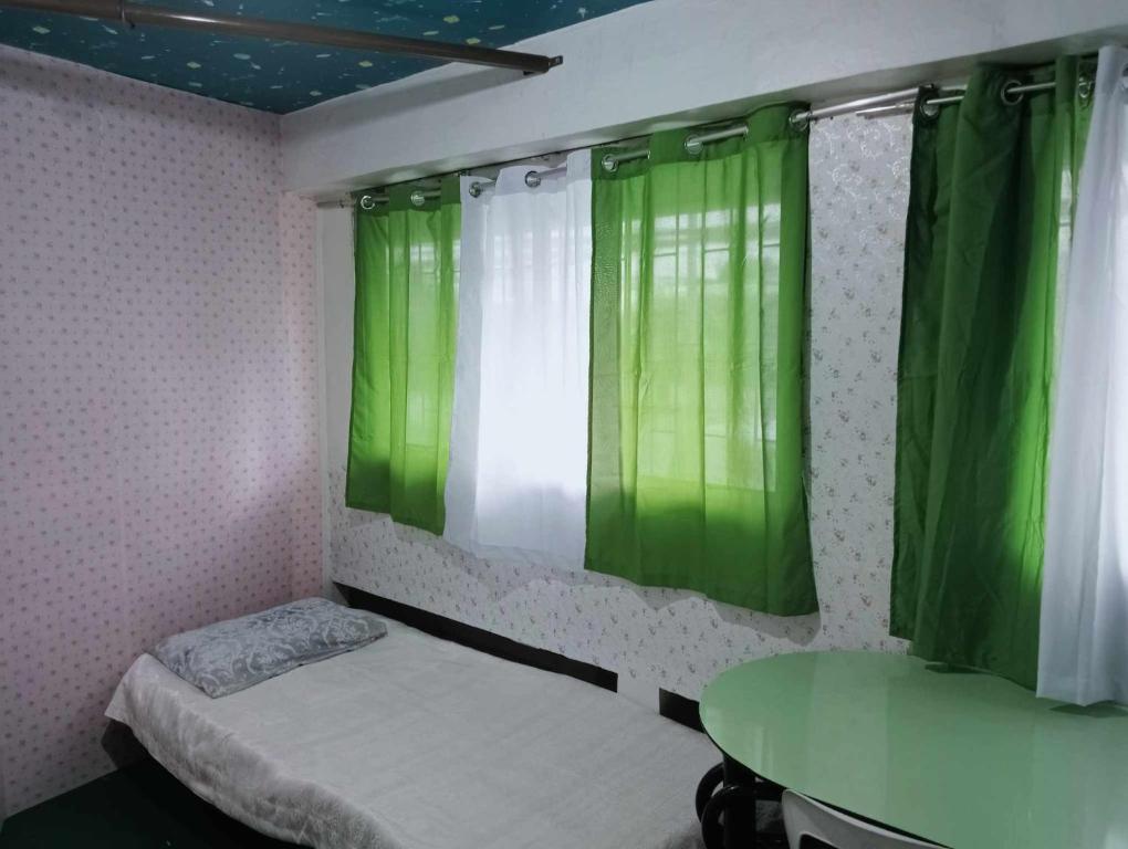 Habitación pequeña con cortinas verdes y mesa. en Quickshape/Quickshield Homestay en Naga