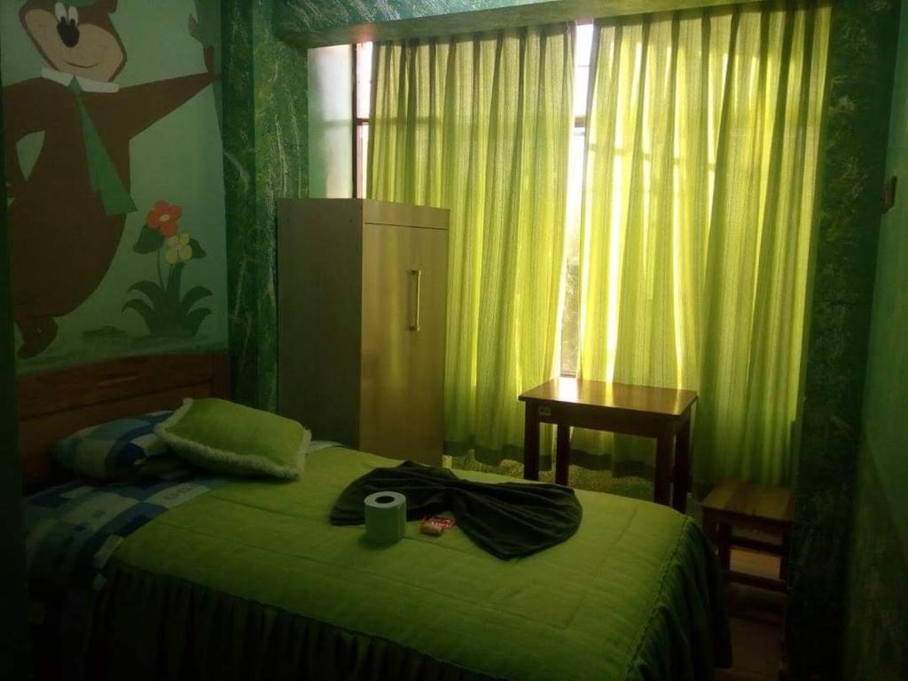 a bedroom with a green bed with a table and a window at Hotel Bethania in Oruro