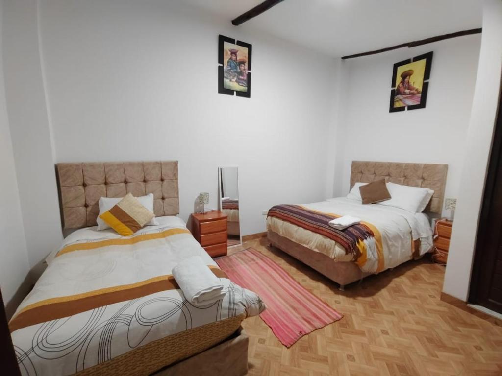 two beds in a room with white walls and wooden floors at CASA DE MELISSA in Ollantaytambo
