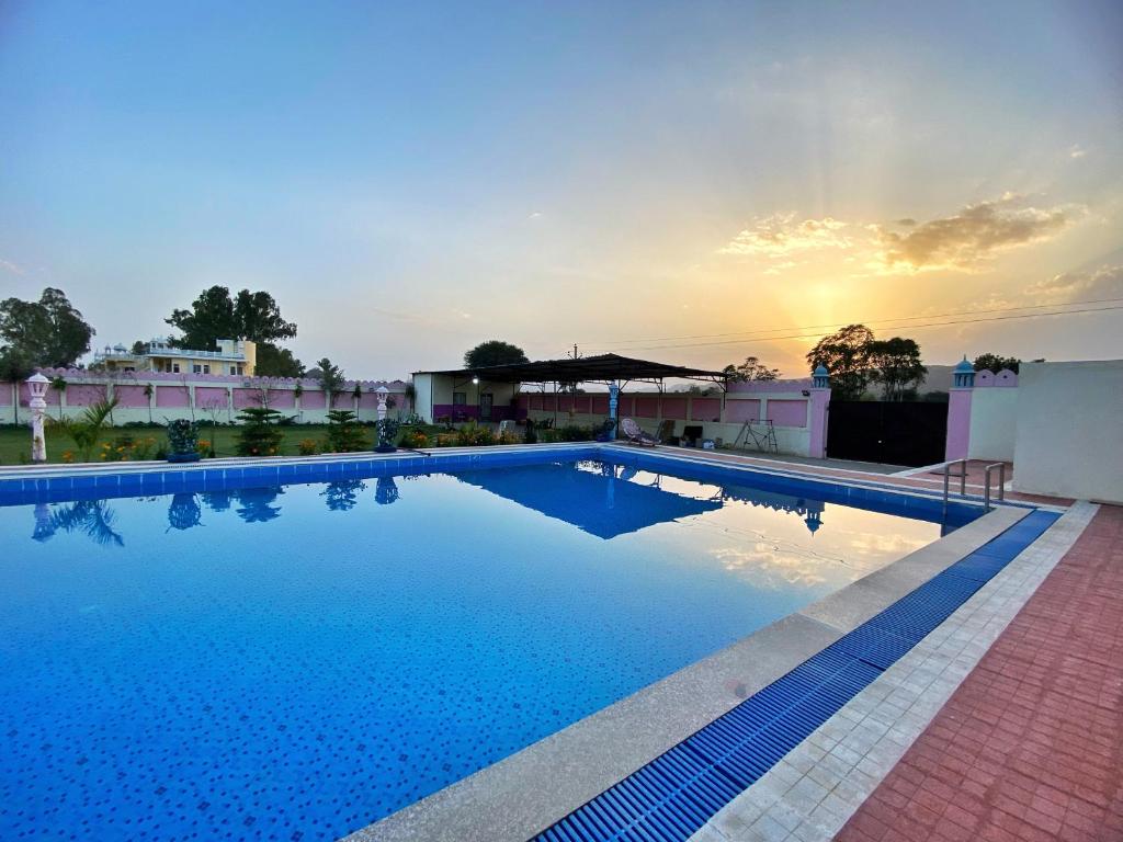 a large swimming pool with a sunset in the background at The Kukas Resort in Jaipur