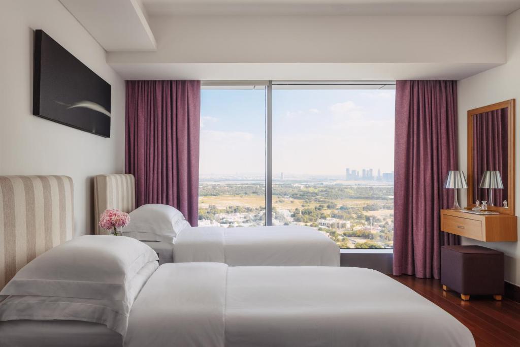 جميرا ليفينغ المركز التجاري العالمي دبي  في دبي: سريرين في غرفة الفندق مع نافذة كبيرة