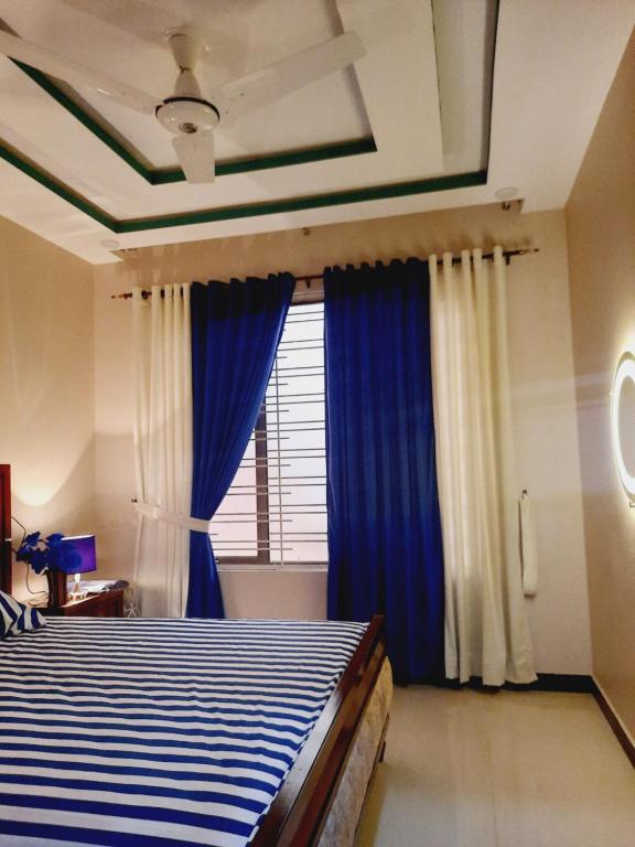 a bedroom with a bed with blue curtains and a window at Dream home 2 & 4 bedroom Family house in Karachi