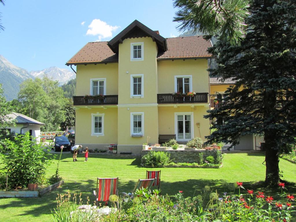 a large yellow house with chairs in the yard at Villa Talheim in Mallnitz