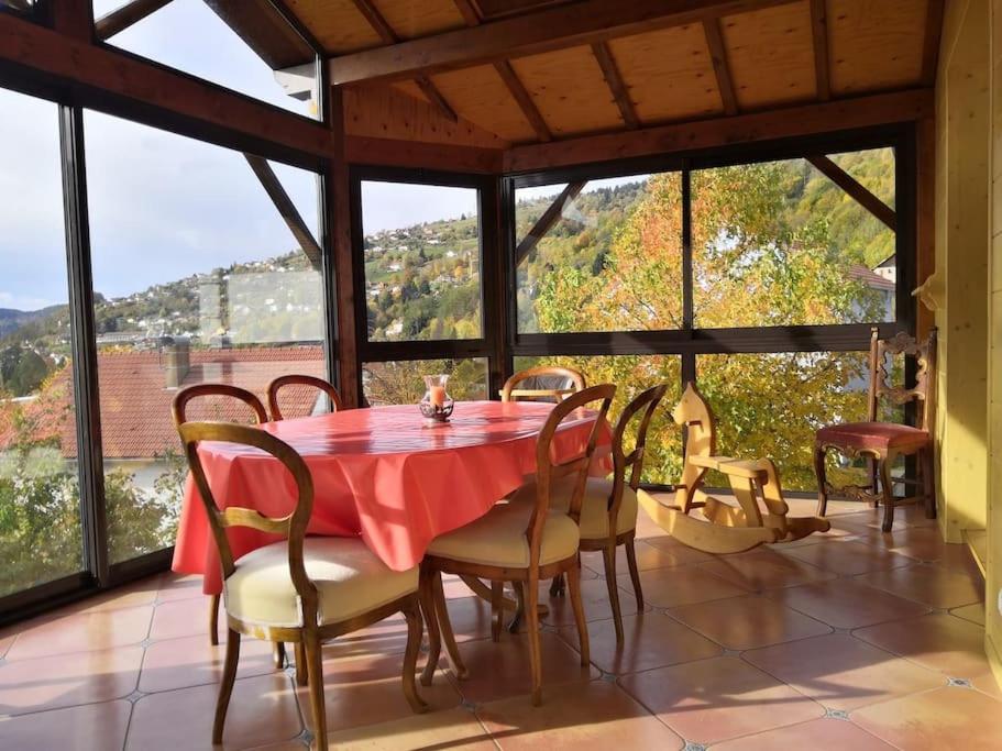 Un comedor con mesa y sillas y ventanas. en La Maison Chamarrée, en La Bresse