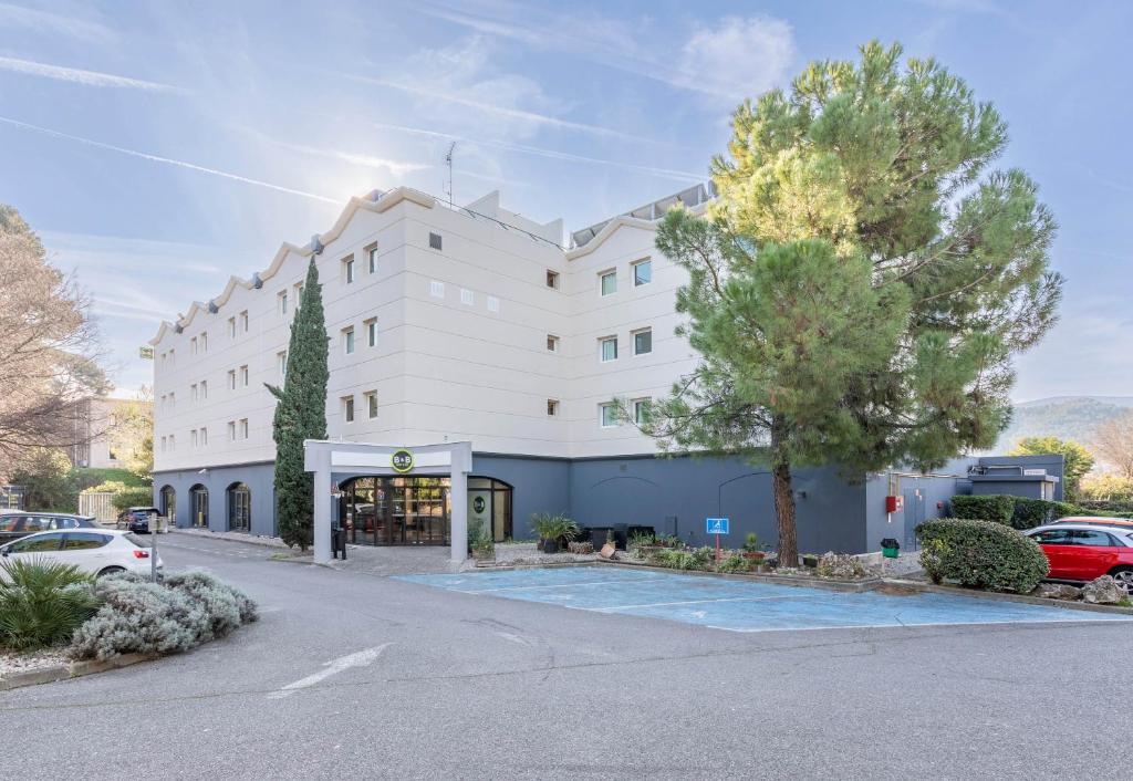 un grand bâtiment blanc avec des voitures garées dans un parking dans l'établissement B&B HOTEL Marseille La Valentine Porte d'Aubagne, à Marseille