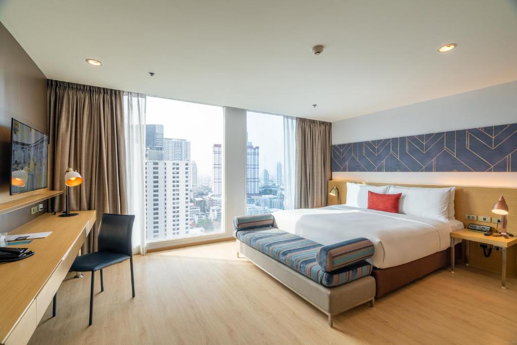 una camera d'albergo con un grande letto e una scrivania di VELA Dhi GLOW Pratunam a Bangkok
