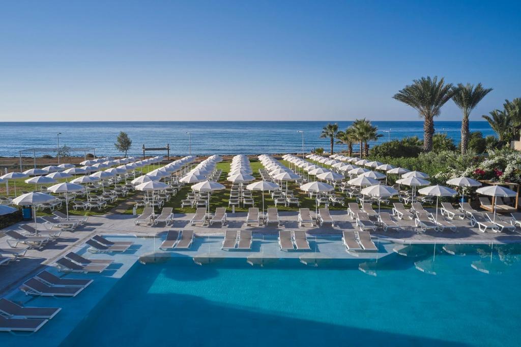 a pool with chairs and umbrellas and the ocean at Atlantica Sungarden Park in Ayia Napa
