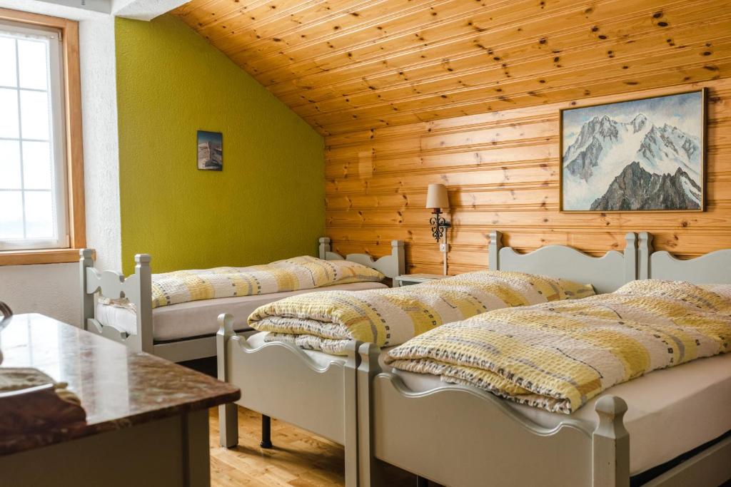 een kamer met 4 bedden in een kamer met houten wanden bij Hotel Chasseral in Nods