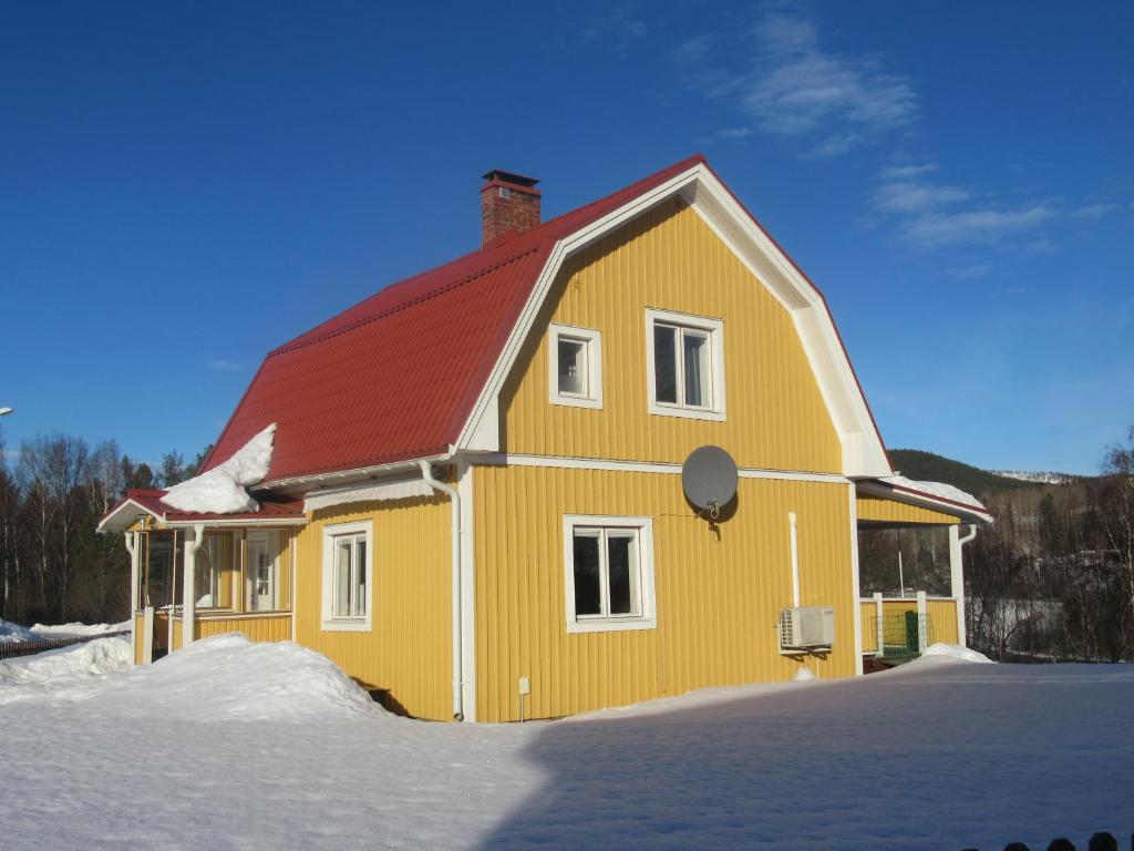une maison jaune avec un toit rouge dans la neige dans l'établissement Villa Indalsälven, à Hammarstrand