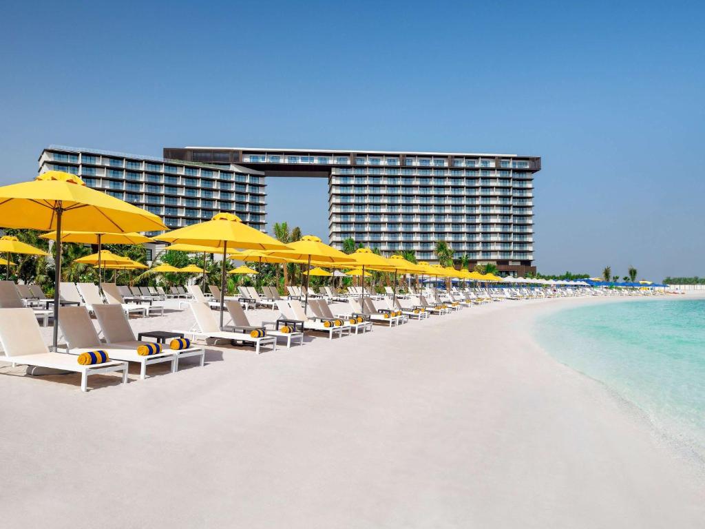 eine Reihe von Stühlen und Sonnenschirmen am Strand in der Unterkunft Mövenpick Resort Al Marjan Island in Ras al Khaimah