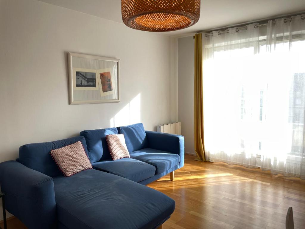 a living room with a blue couch and a large window at Chaleureux nid au cœur du village Olympique in Saint-Denis