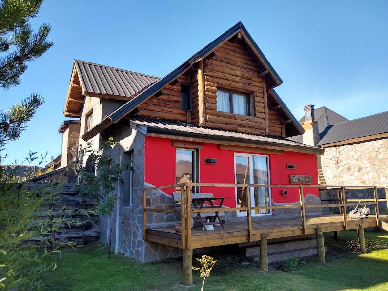 a red house with a wooden deck with a table at La Andyna Caviahue in Caviahue
