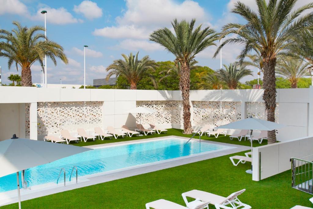 a swimming pool with chairs and palm trees at Port Elche in Elche