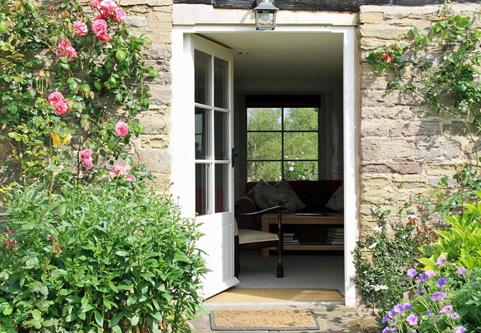 赫里福德的住宿－Dee's Cottage at Brinsop，一座带椅子和鲜花的房子的敞门