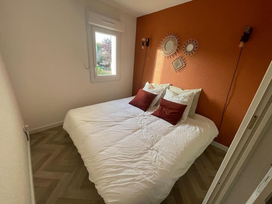 un letto con lenzuola bianche e cuscini rossi in una camera da letto di Appartement Cap d'Agde dans résidence avec piscine a Cap d'Agde