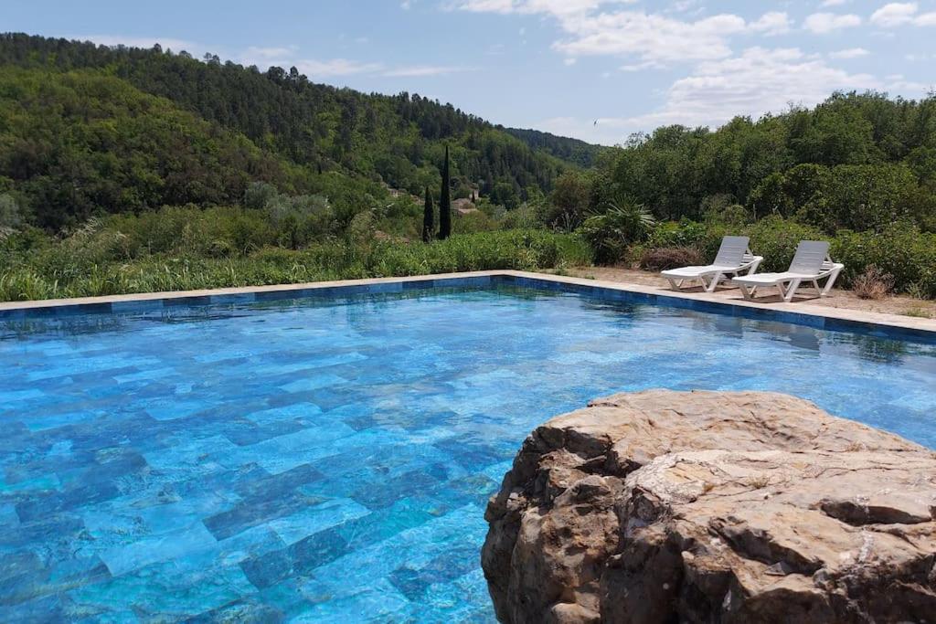 - une piscine avec 2 chaises et un rocher dans l'établissement Mas Anahata - Gîte Shanti, au coeur de la nature, à Générargues