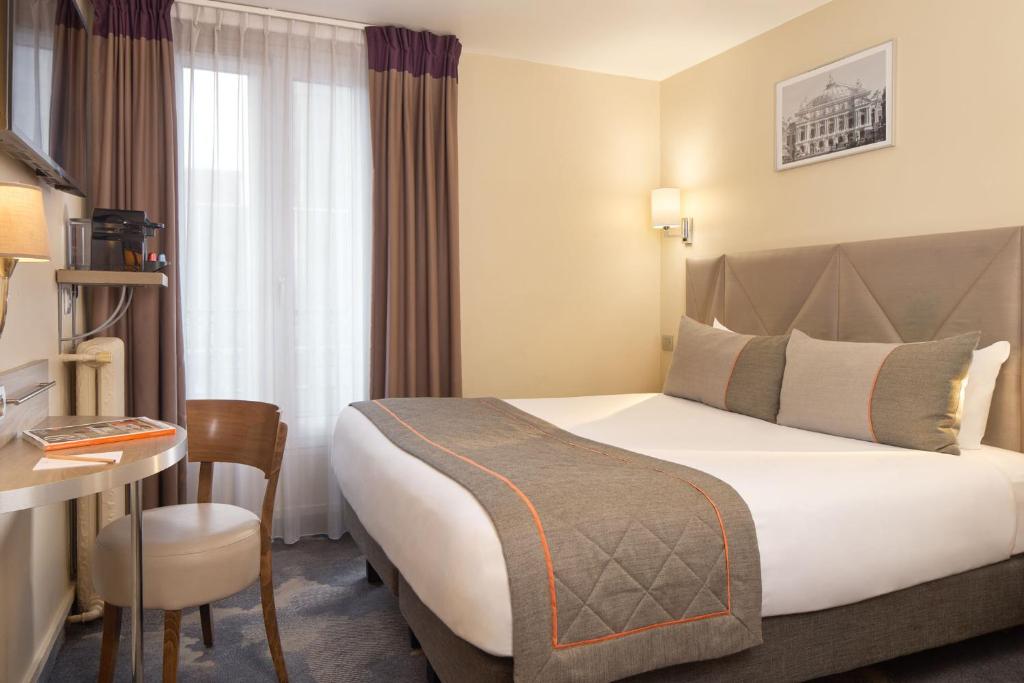 パリにあるティムホテル モンパルナスの大きなベッドとデスクが備わるホテルルームです。