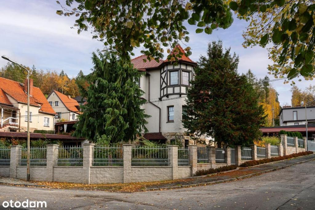 a white house with a fence in front of a street at Apartament Rubinowy in Polanica-Zdrój