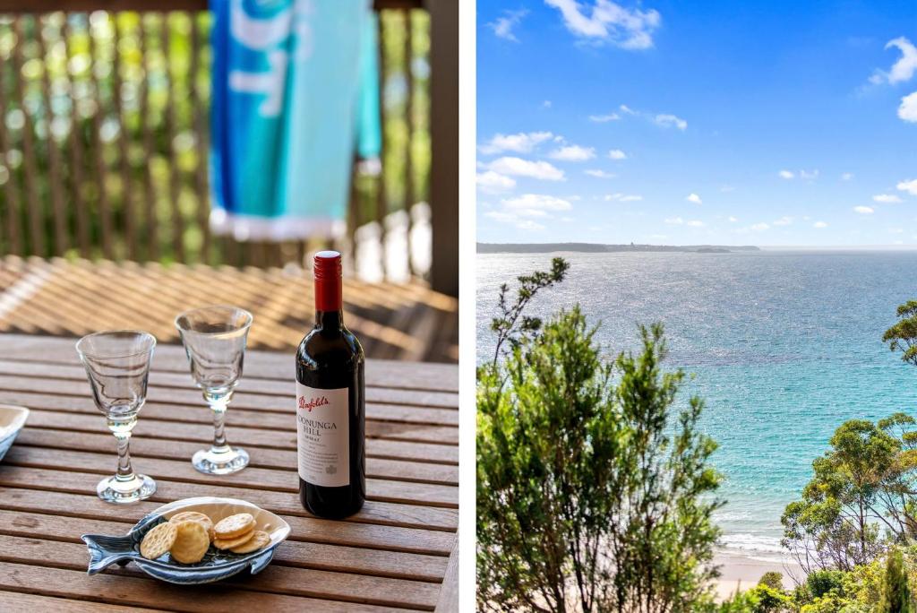 a bottle of wine and glasses on a table with the ocean at Sapphire Views - Narrawallee Beach in Narrawallee