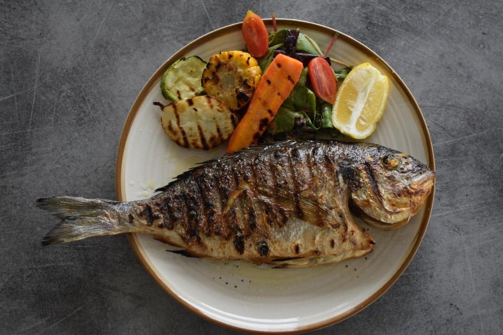 a plate of food with a fish and vegetables at Afrodite Seaside Rooms in Kallithea Halkidikis