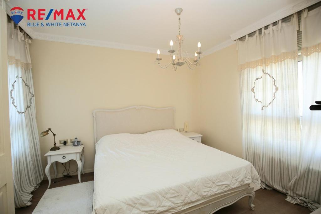 um quarto branco com uma cama branca e um lustre em פנינה על הים em Netanya