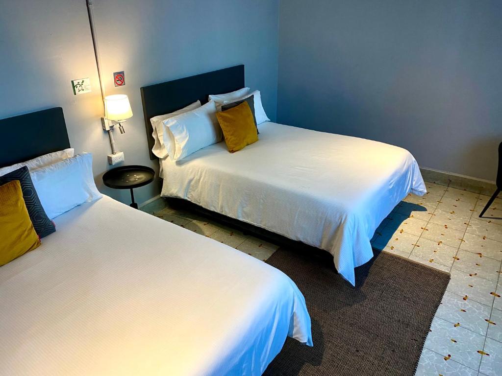 um quarto de hotel com duas camas com lençóis brancos e almofadas amarelas em EL PEDREGAL HOTEL em Matehuala