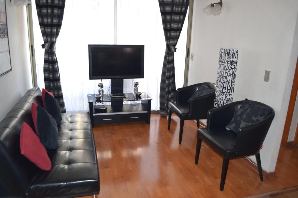 Sala de estar con 2 sillas de cuero negro y TV en Departamentos Amoblados La Hermandad, en Antofagasta
