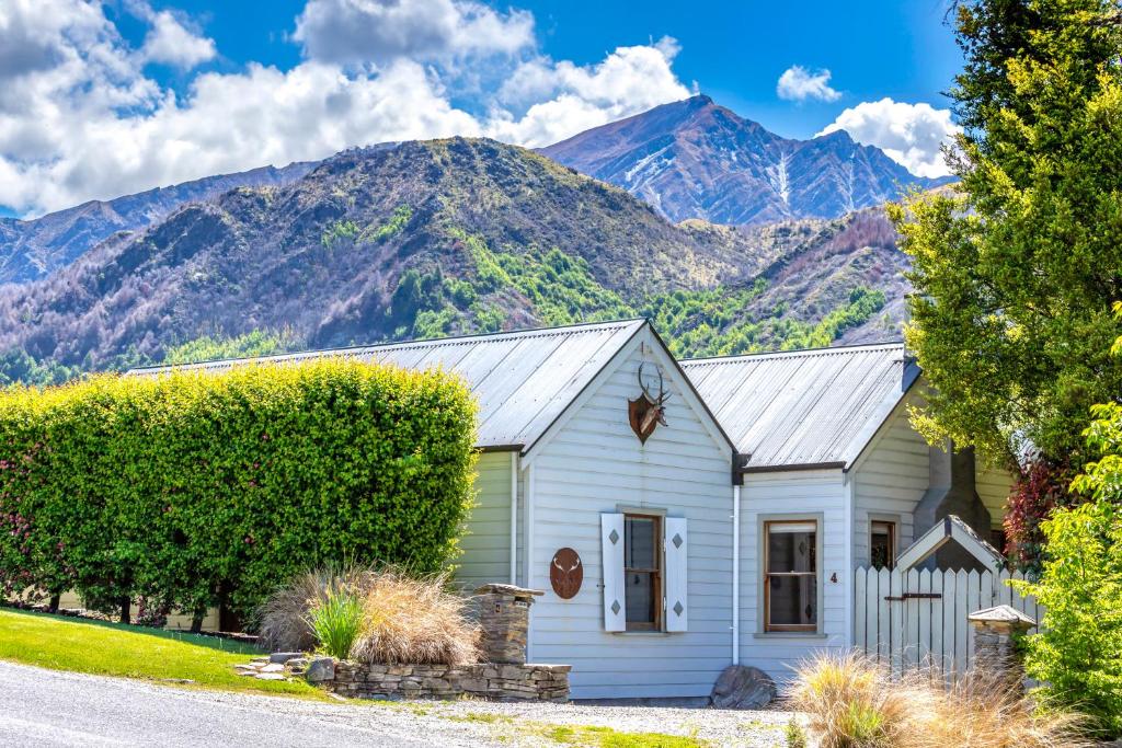 a white house with mountains in the background at Stags Head Cottage-cosy cottage with hot tub in Arrowtown