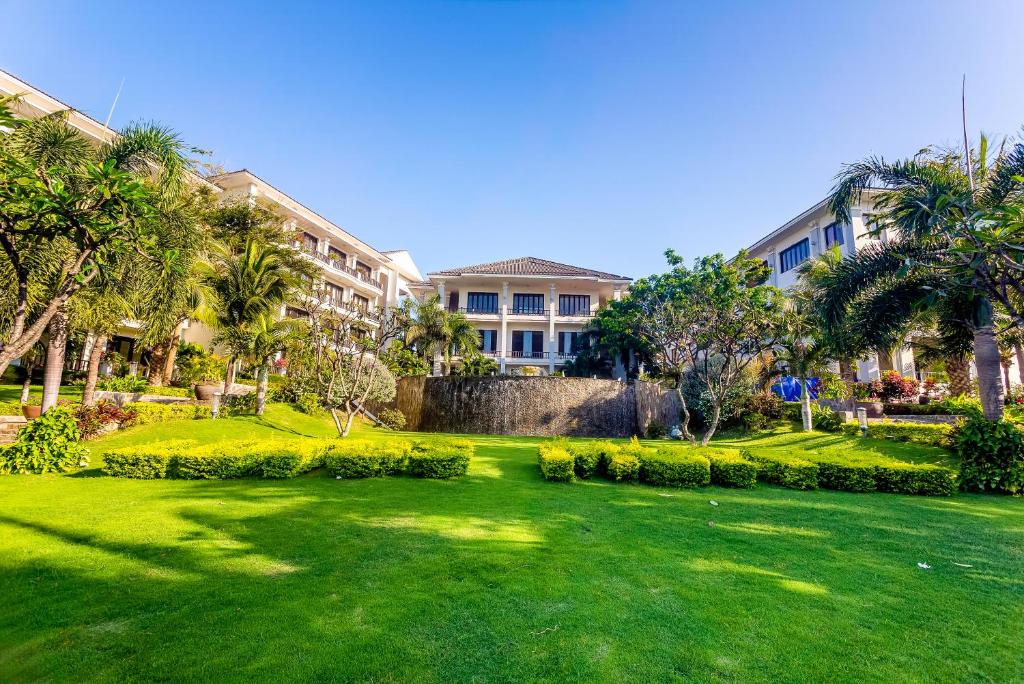 a green lawn in front of a building with palm trees at Lotus Muine Resort & Spa in Mui Ne