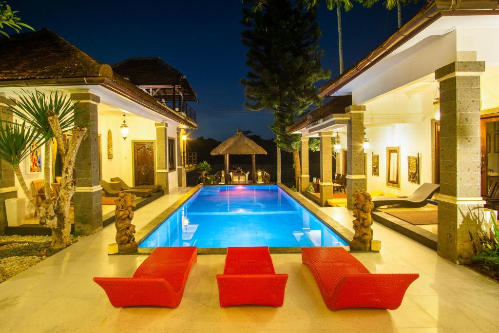 Balam Bali Villa في Mengwi: مسبح وكراسي حمراء ومنزل