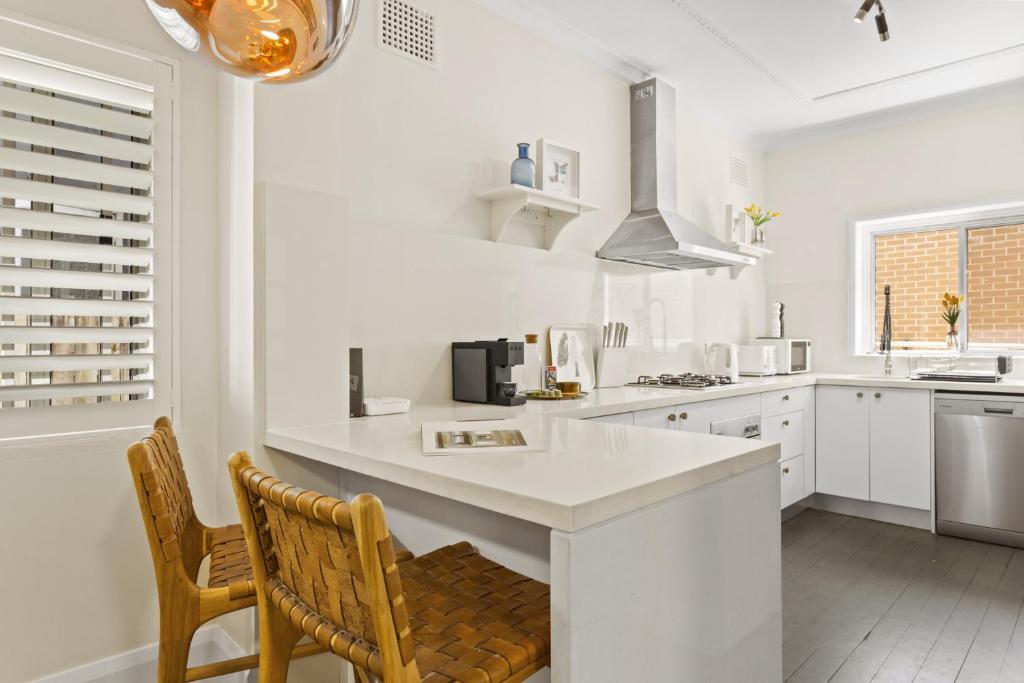 eine weiße Küche mit einer Theke und 2 Stühlen in der Unterkunft Comfy 2-Bed Apartment with AC throughout in Sydney