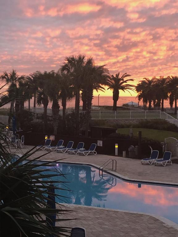 a pool with chairs and palm trees at sunset at Gulfside 210 - 2BR plus bunkroom with Ocean & Pool Views in Fort Walton Beach