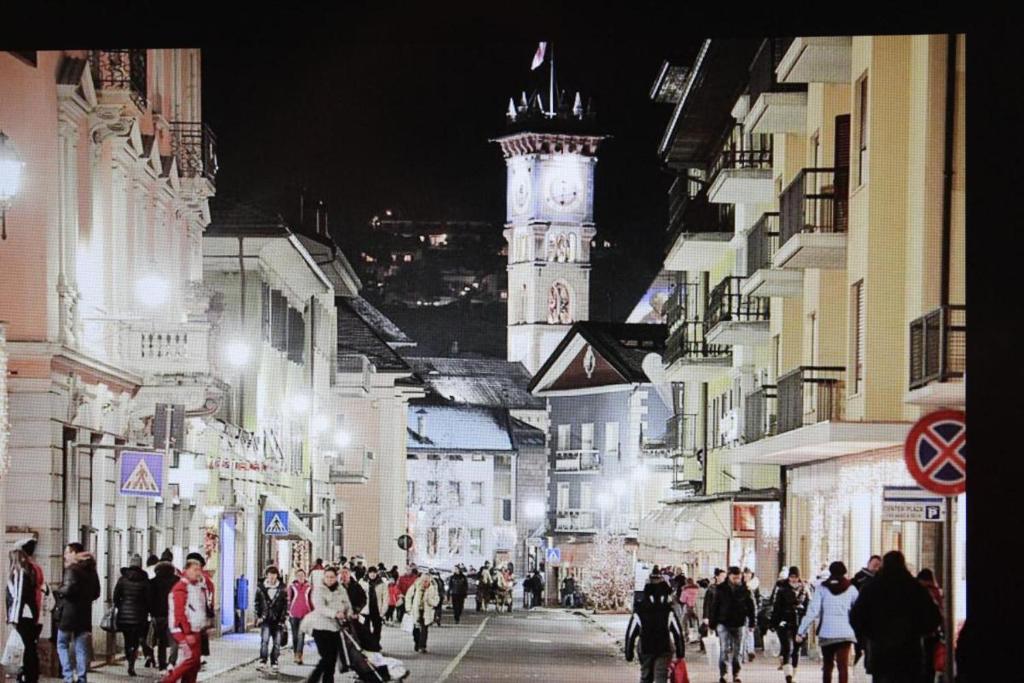 Una folla di persone che camminano per strada con una torre dell'orologio di Suite Marco, Cavalese. CIPAT 022050-AT-993709 a Cavalese