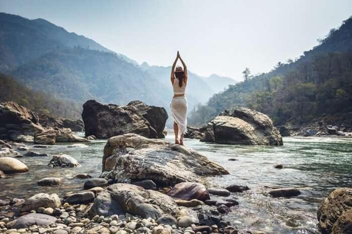 瑞詩凱詩的住宿－Rishikesh Shiv Dham Homestay，站在河边岩石上的身着白色衣服的女人