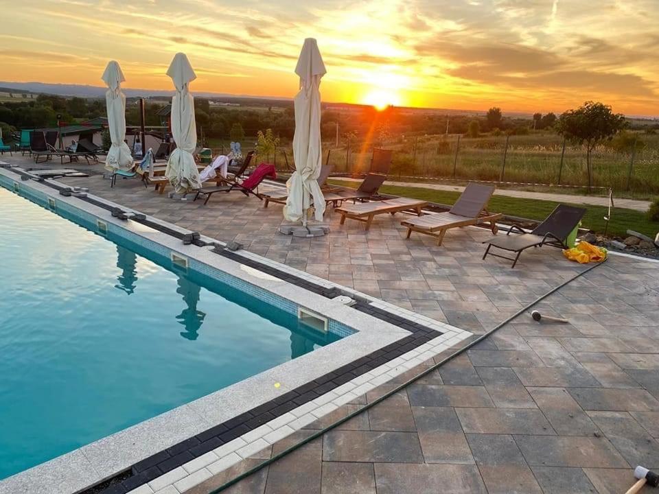 una piscina con sedie e ombrelloni e il tramonto di Complex Turistic Dávid a Boghiş