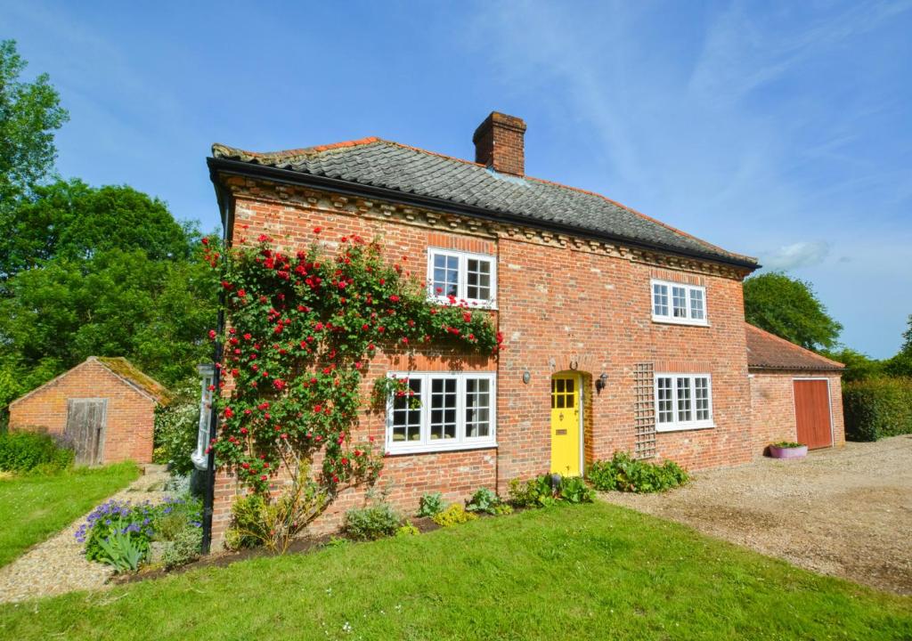 a brick house with a bush with red roses at Clare Cottage in Melton Constable