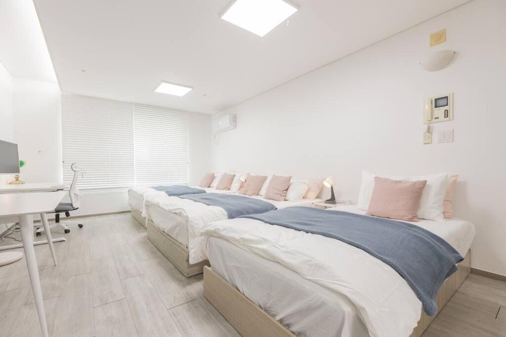 a white bedroom with two beds and a desk at Mirae_stay 33 New Open [2 Queen+1 S-Single] in Seoul