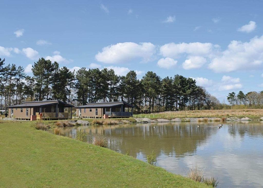 a couple of houses next to a river at Woodhall Country Park Lodges in Woodhall Spa