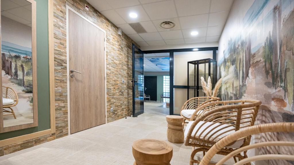 a lobby with wooden chairs and a stone wall at Kyriad Prestige Residence & Spa Cabourg-Dives-sur-Mer in Dives-sur-Mer