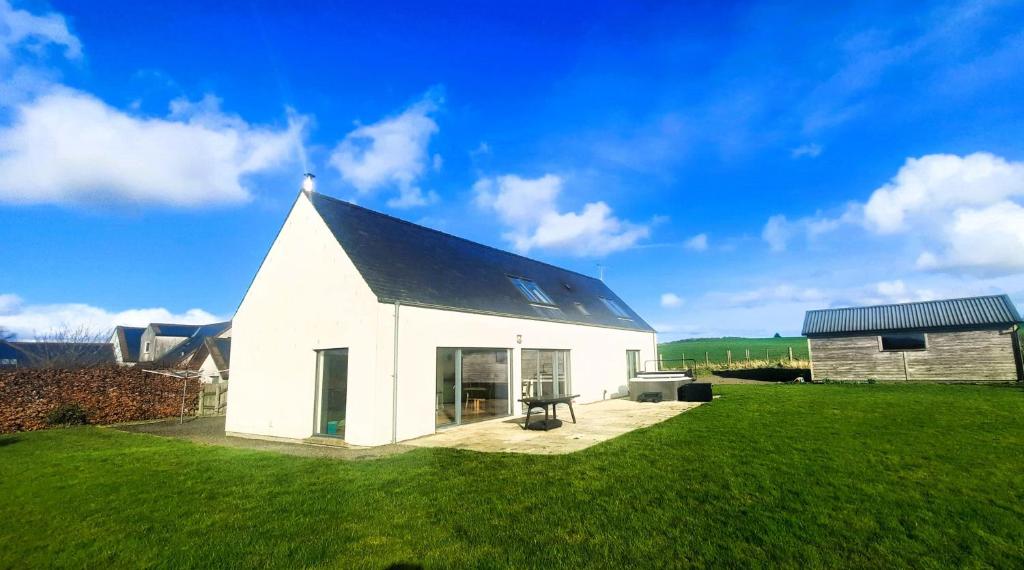 a white house with a black roof on a green field at The Longhouse in Castle Douglas