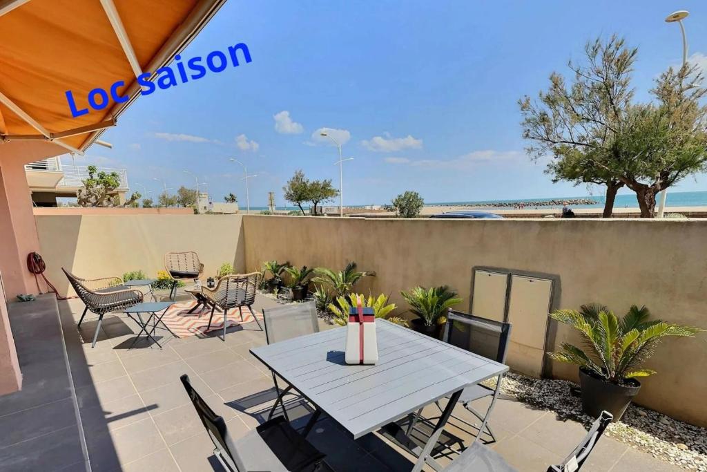 een patio met een tafel en stoelen en het strand bij Sublime appartement face à la mer in Valras-Plage