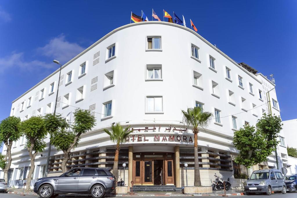 a white building with cars parked in front of it at Hotel Mamora Kénitra in Kenitra