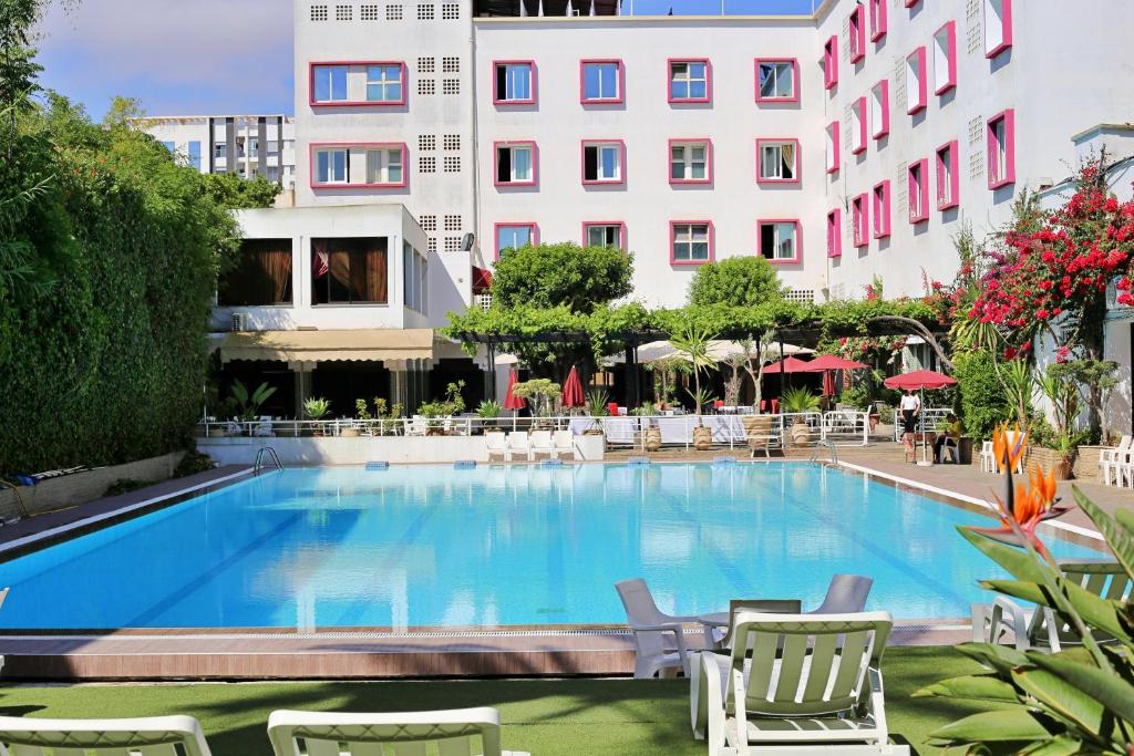 a large swimming pool with chairs and a building at Hotel Mamora Kénitra in Kenitra