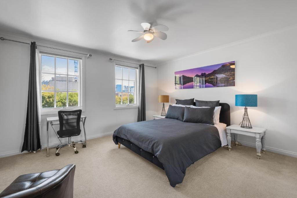 a bedroom with a bed and a chair and windows at Hobart City Townhouse in Hobart