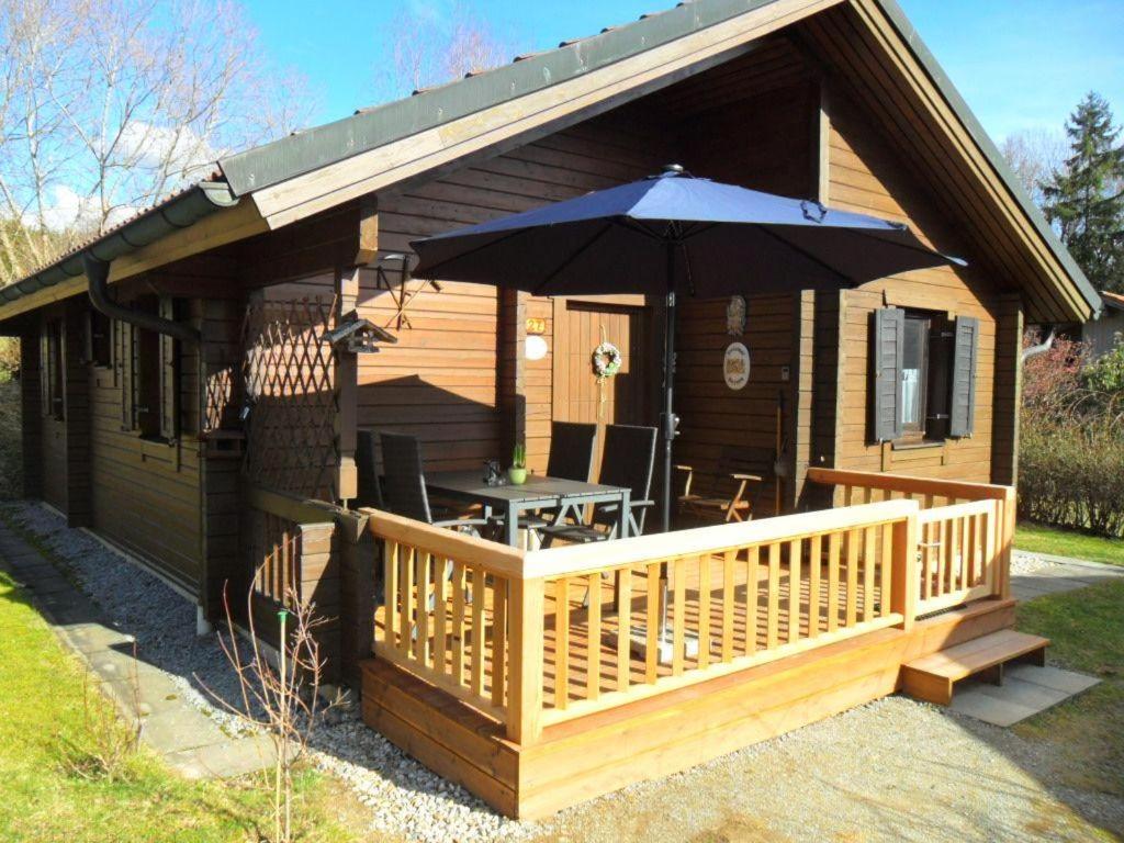 a small cabin with a deck with an umbrella at Komfortables-Ferienblockhaus-Nr-27-56-qm-bis-4-Personen-Viechtach-Jaegerpark in Viechtach