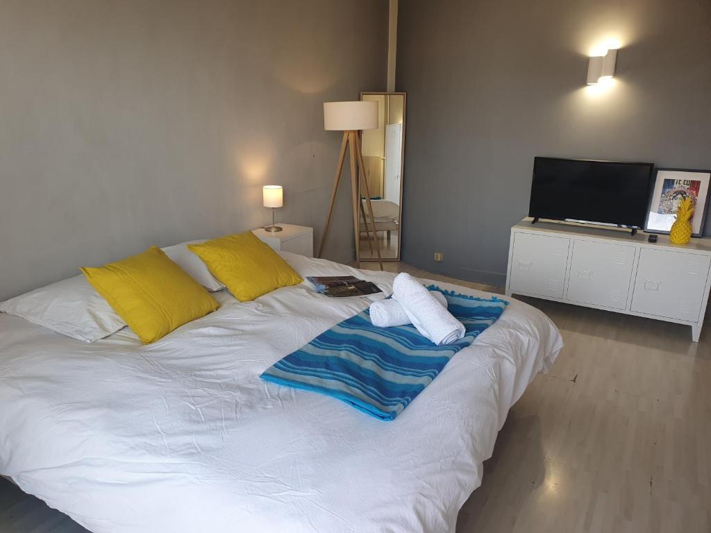 a large white bed with yellow pillows and a television at Vue sur Paris in Ivry-sur-Seine